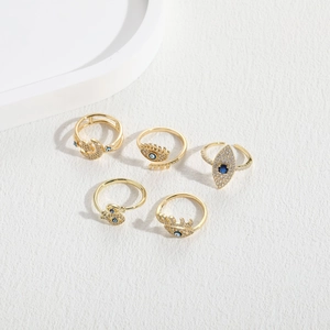 Detailed close-up of five golden evil eye rings with blue zircon on white textured background