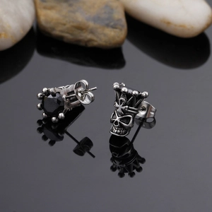 Detailed macro of punk skull and crown earrings with black gemstone inlay