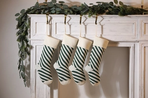 Detail of four green and white striped knitted Christmas stockings on a white fireplace