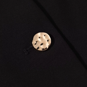 Dettaglio macro di un bottone dorato martellato su un blazer nero da donna elegante