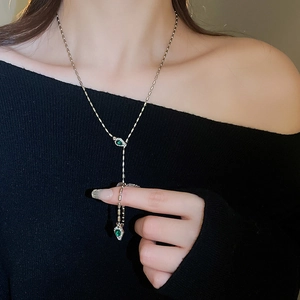Detail of Y-shaped gold snake chain necklace with emerald green gemstone drop pendants