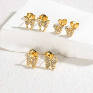 Detail of three pairs of gold butterfly earrings with cubic zirconia on white stone