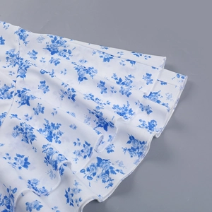 Dettaglio di un abito bianco con stampa floreale blu e bordi con volant a più strati
