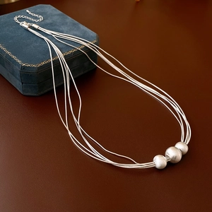 Multi-strand silver beaded necklace with brushed metallic pendants on leather background