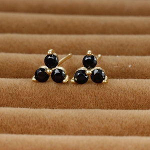 Detailed macro view of golden clover studs with black gemstones on velvet tray