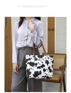 Detailed view of cow print tote bag with brown handles and golden metal buckle