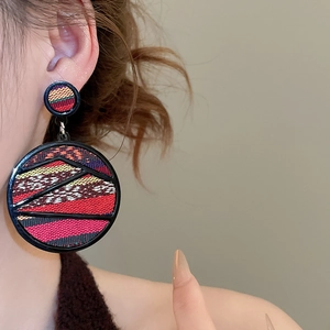 Close-up of bohemian oversized round earrings with colorful woven texture on a model