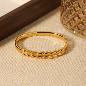 Golden wheat-patterned stainless steel bangle with polished finish on warm background