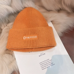 Vibrant orange knit beanie with white embroidered patch on a soft textured background
