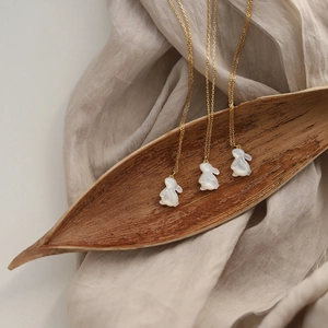 Trois colliers dorés avec pendentifs lapin blanc posés sur des feuilles d'automne
