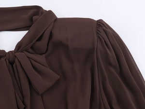 Dettaglio di un abito in chiffon marrone scuro con scollo a fiocco e spalla con pieghe fini