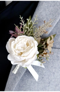 Detailed view of a cream white boutonniere with greenery on a light grey suit lapel