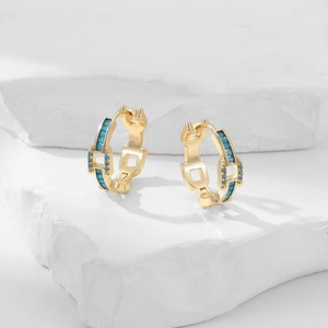 Detail of gold-plated hoop earrings with turquoise stones on a white stone background