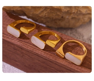 Three 18K gold-plated titanium steel rings with white shell inlay on a dark wood base