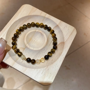 Détail macro d'un bracelet en perles d'oeil de tigre et citrine sur plateau bois