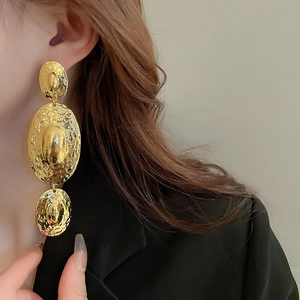 Detailed view of hammered golden triple-link oval earrings worn on a model's ear
