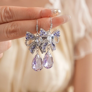 Close-up of elegant silver bow earrings with purple teardrop crystals on model's ear