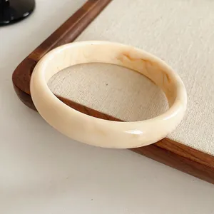 Minimalist cream resin bangle with brown marble texture shown on a rustic wooden tray