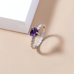 Macro detail of a silver ring featuring a purple heart gemstone and twisted band design