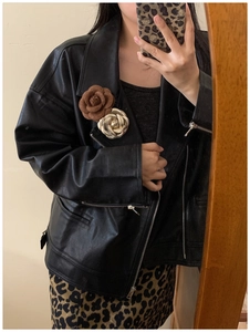 Close-up of floral brooch with fabric and metal roses on a black leather jacket