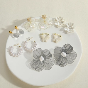 Detailed set of six pairs of gold and white floral earrings on a white tray