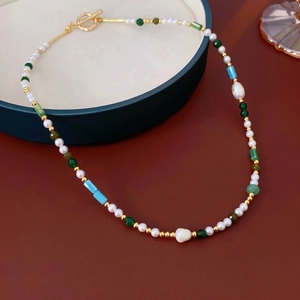 Elegant pearl necklace with colorful beads and gold OT clasp on deep green tray