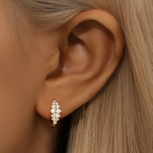 Close-up of golden cluster earrings with white cubic zirconia crystals worn by a model