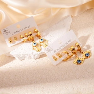 Detail view of gold stainless steel evil eye and hamsa hand earrings set on satin