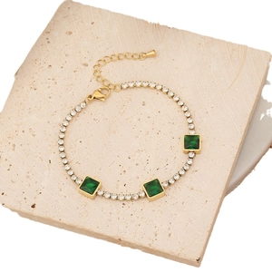 Gold tennis bracelet with square green stones and white cubic zirconia on stone surface