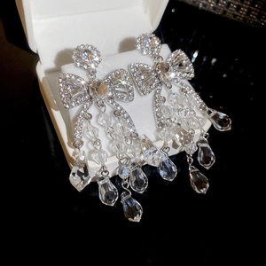 Macro shot of silver bow tassel earrings with sparkling crystals on a black velvet box