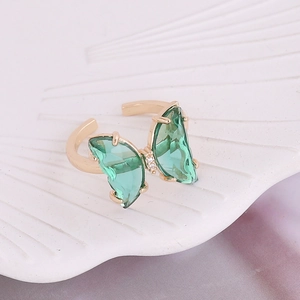 Macro view of adjustable gold butterfly ring with green glass wings on a shell tray
