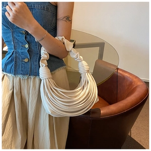Chic beige pleated underarm bag with unique woven texture held by a model in a stylish room