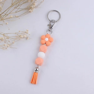 Vue détaillée des perles en silicone orange, du charme fleur et du porte-clés à pompon orange