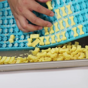 Detail showing blue silicone mold for releasing bone-shaped dog treats onto a tray