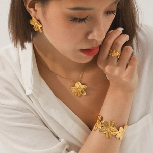 Model wearing gold flower jewelry set including necklace, earrings, ring and bracelet