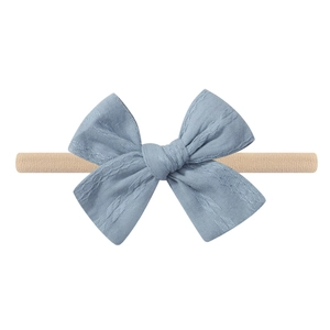 Detail of baby headband with dusty blue textured bow on a beige elastic nylon band