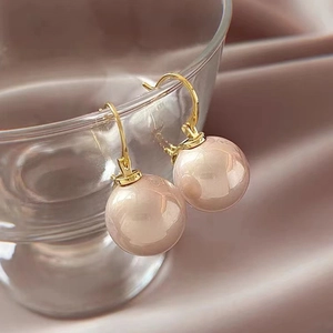 Elegant gold-plated pearl drop earrings displayed on a glass rim with silk background