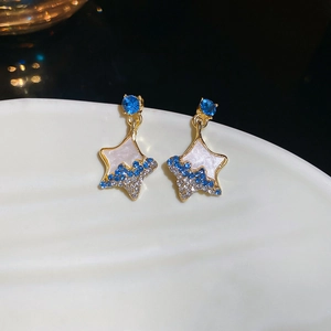 Detail of star-shaped pendant earrings with blue rhinestones on a white shell plate