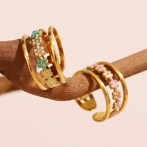 Artistic display of floral enamel rings on wood with pink background detail