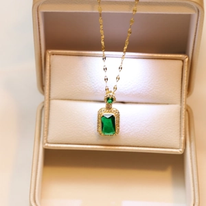 Close-up of gold necklace with green rectangular gemstone and crystals in a jewelry box