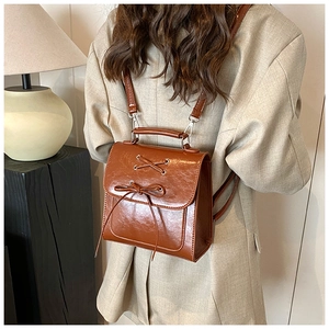 Detail of retro brown leather mini backpack featuring cross straps and decorative bow