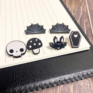 Detail of wooden Halloween skull, bat, and mushroom earrings on a notebook background