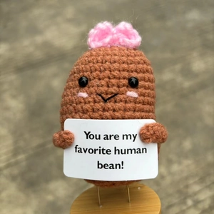 Close-up of handmade brown crochet bean doll holding a tiny sign with sweet message
