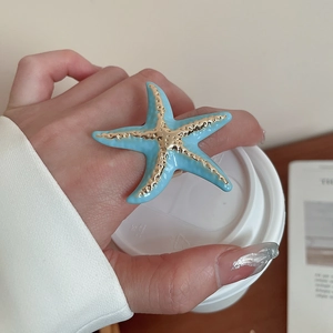 Detailed close-up of blue enamel starfish ring with golden accents on a hand
