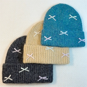Winter knitted beanie hats with ribbon bows in blue, beige, and dark grey colors