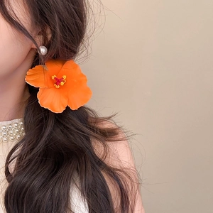 Detail view of a vibrant orange fabric hibiscus hair clip worn by a model for vacation styling