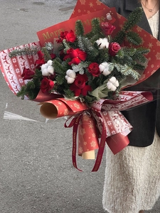 Christmas bouquet with red roses, cotton, and Nobilis pine branches held outdoors