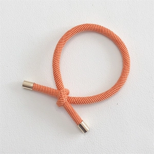 Detail of coral orange braided hair tie featuring a center knot and gold metal end caps