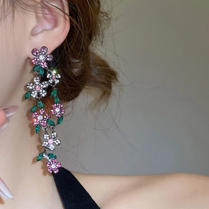 Close-up of sparkling floral tassel earrings with pink and green crystals on model