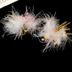 Detail of white feather earrings with dried flowers and small gold bells on black base
